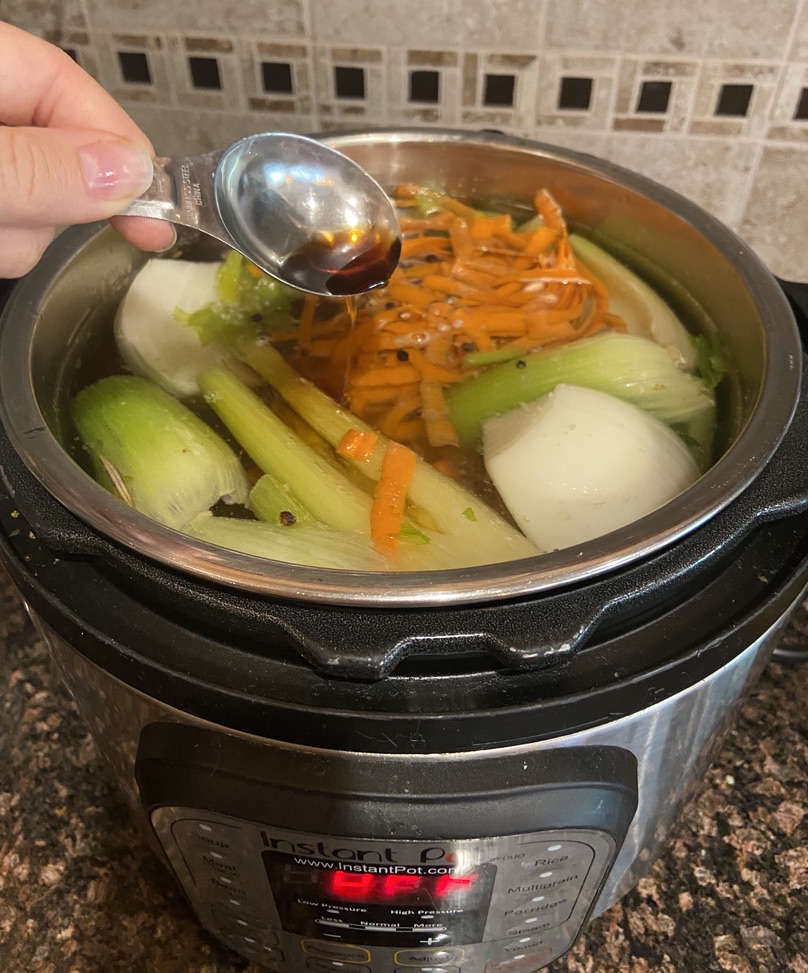 woman's hand pouring fish sauce into bone broth instant pot before cooking