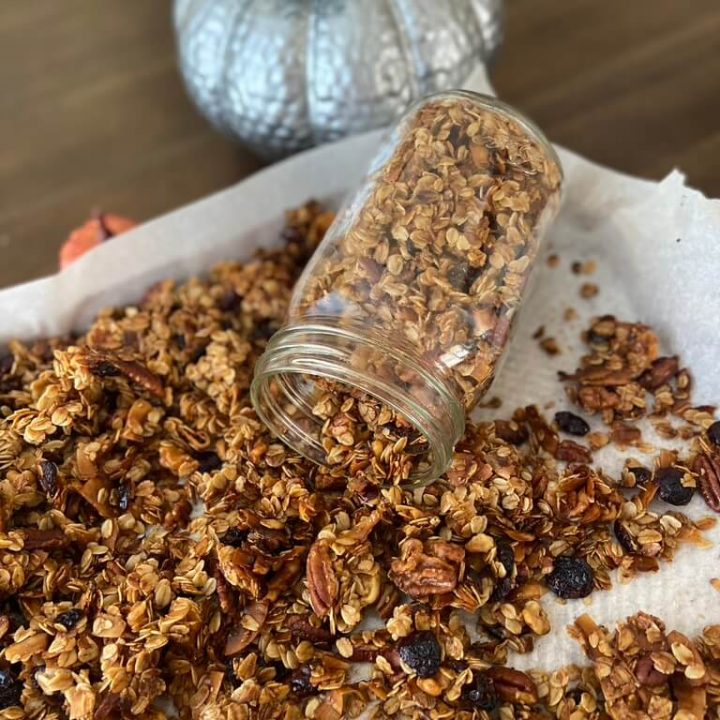glass jar of pumpkin spice granola spilled on cookie sheet with decorative pumpkins in background