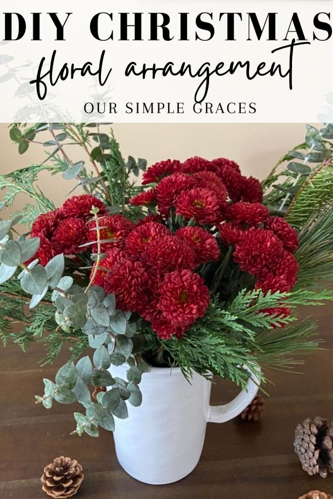Image of red mums and greener in a white pitcher sitting on dining table with pine cones around and text above image describing the DIY flower arrangement