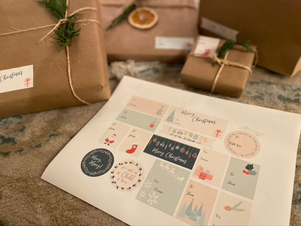image of printed out christmas sticker gift tags and packages behind wrapped in kraft paper twine and greenery