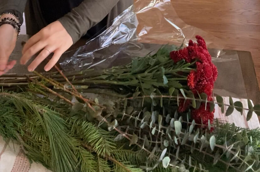 image of woman laying out bunch of red mums, eucalyptus, and pine and cedar bundles on kitchen towel on table