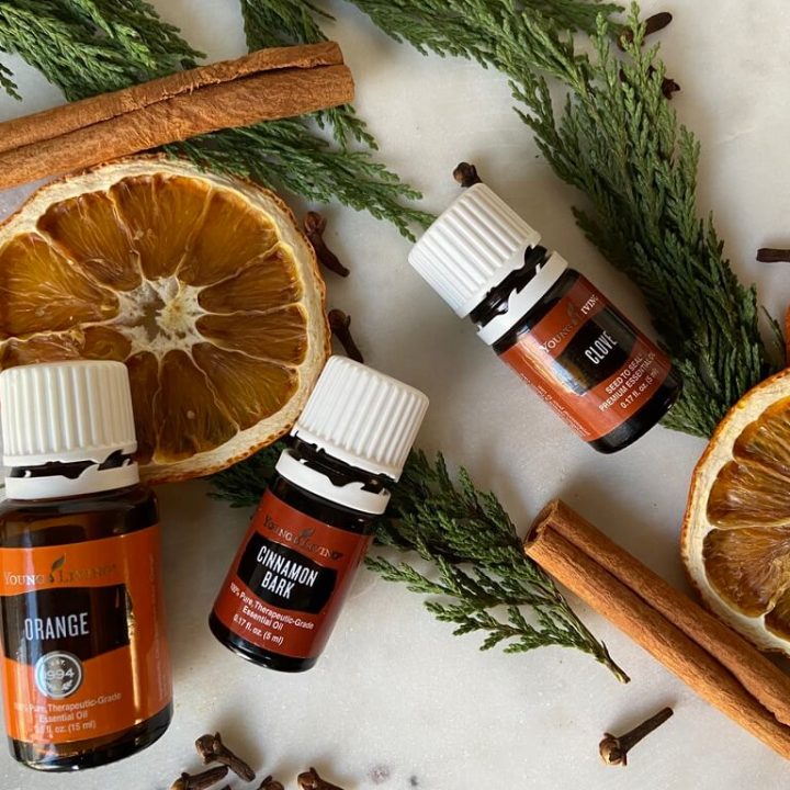 image of essential oils laying on marble top with oranges and cinnamon and greenery underneath bottles