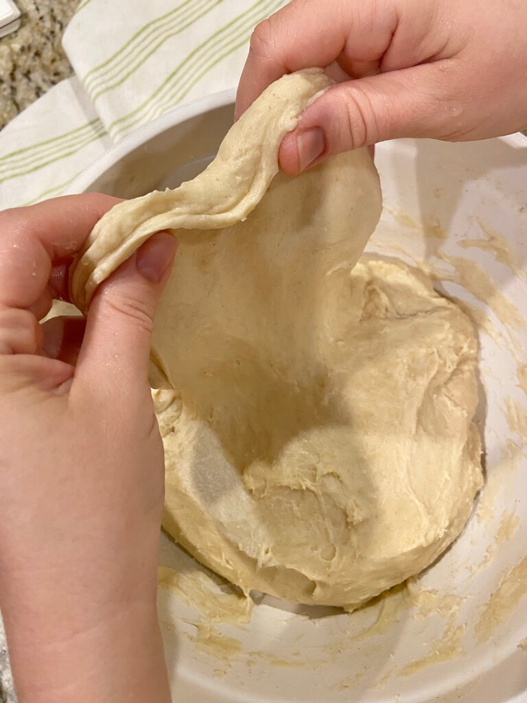 image of woman's hands stretching sourdough dough up in a white bowl