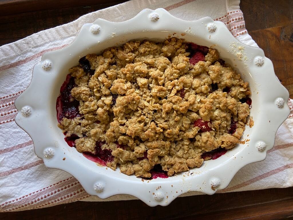 image of baked mixed berry crisp in white scalloped baking dish on kitchen towel