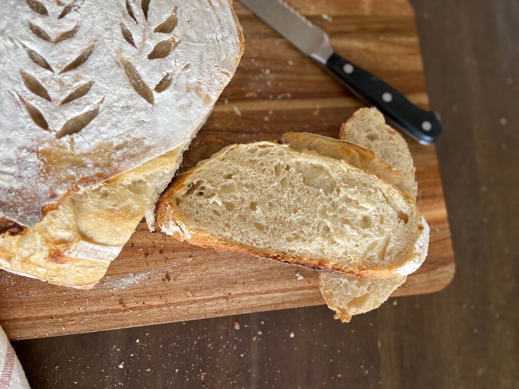 sourdough bread loaf slices on wood cutting board and bread knife in background