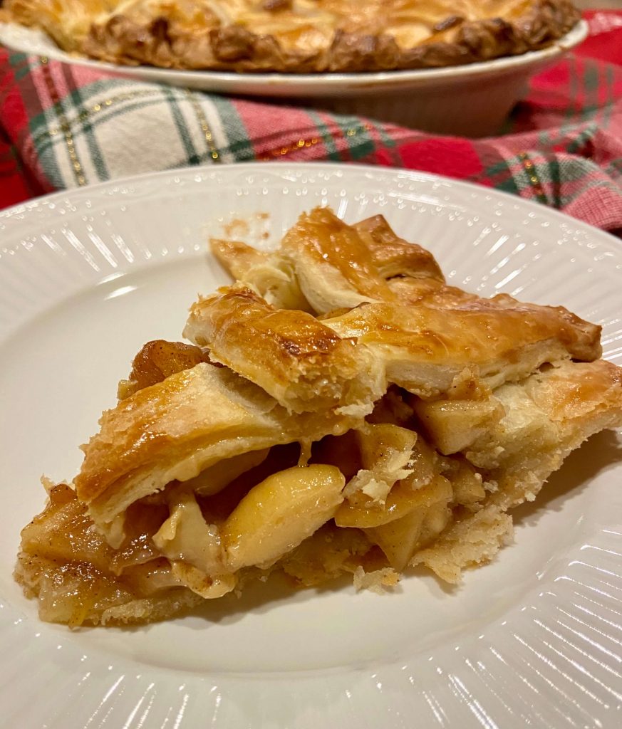 slice of apple pie with lattice top on white plate and kitchen towel in background