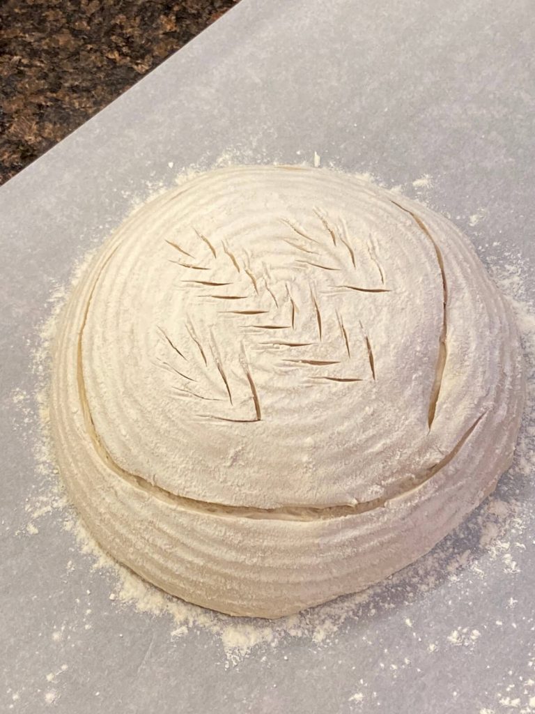 close up image of unbaked sourdough boule scored with design