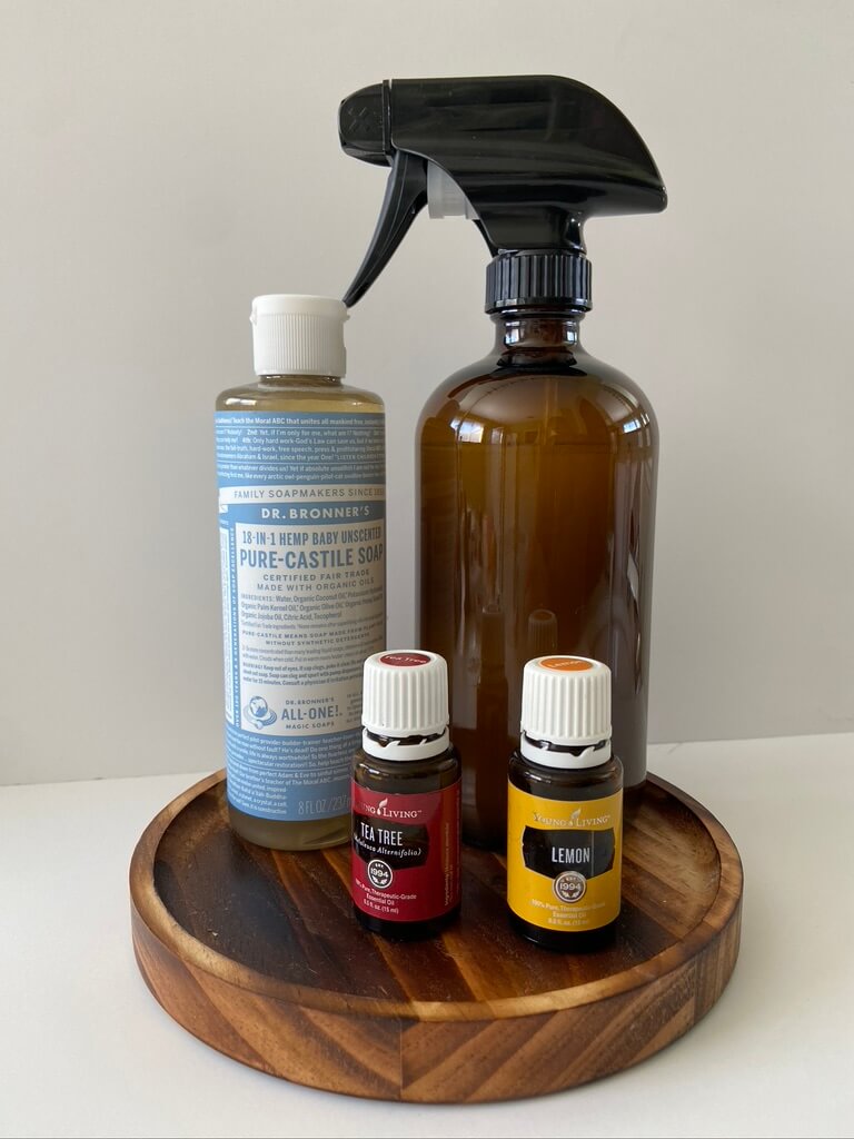 castile soap tea tree and lemon essential oils and amber glass spray bottle on wood plate