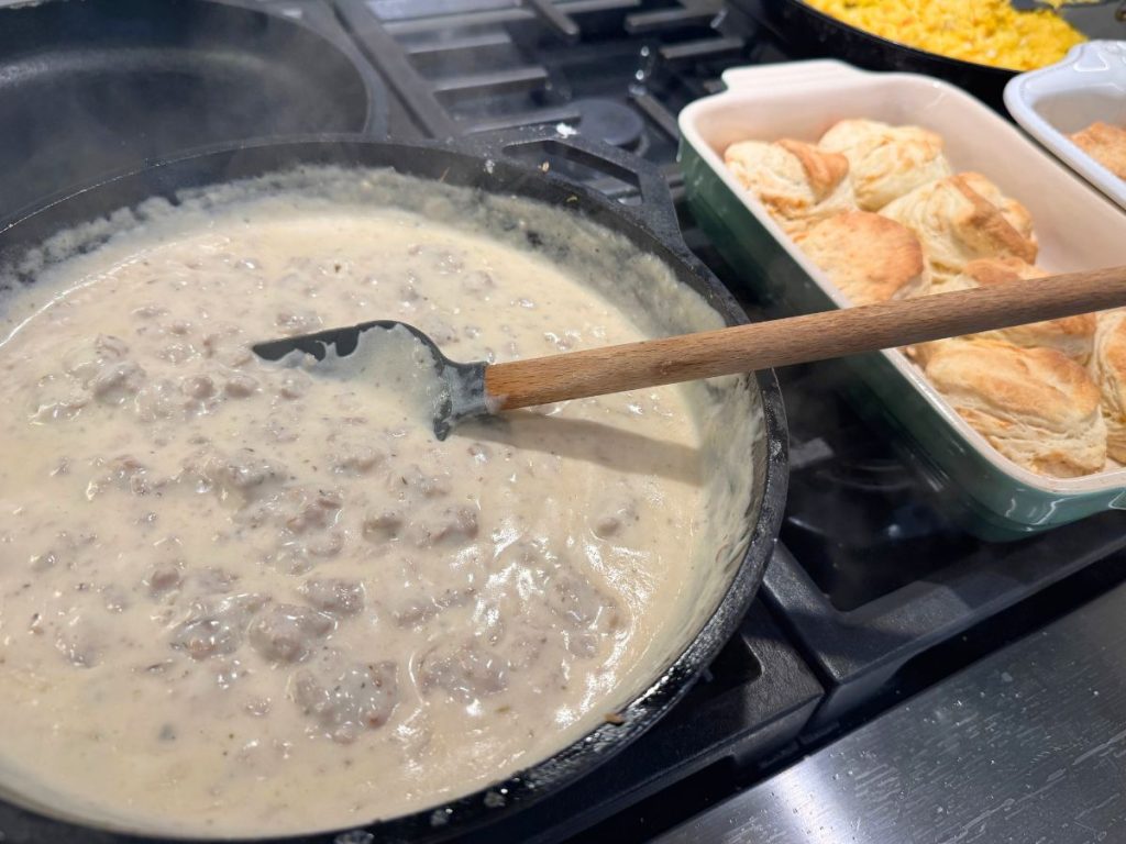 stove top cooking sausage gravy with biscuits and eggs in background